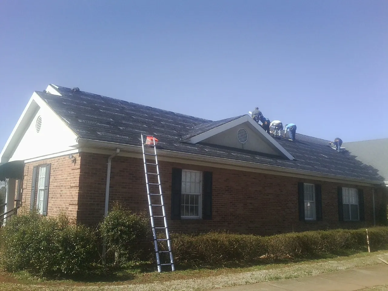 Crew tearing shingles off a brick ranch roof with a ladder set — Metal Roof Repair work by our crew in Walbridge