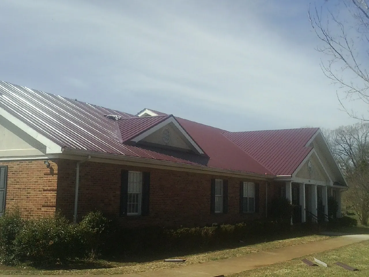 Red metal roof with gabled entries on a long brick building, from a Hail Damage Roof Repair job in Walbridge