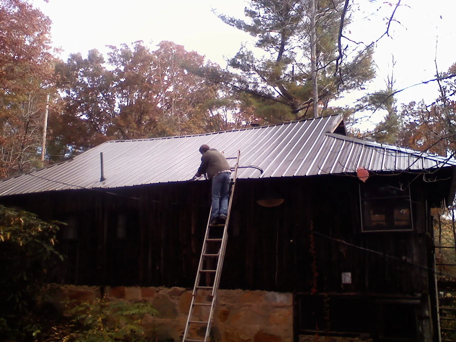 Roofer on a ladder working along the edge of a cabin metal roof in Walbridge