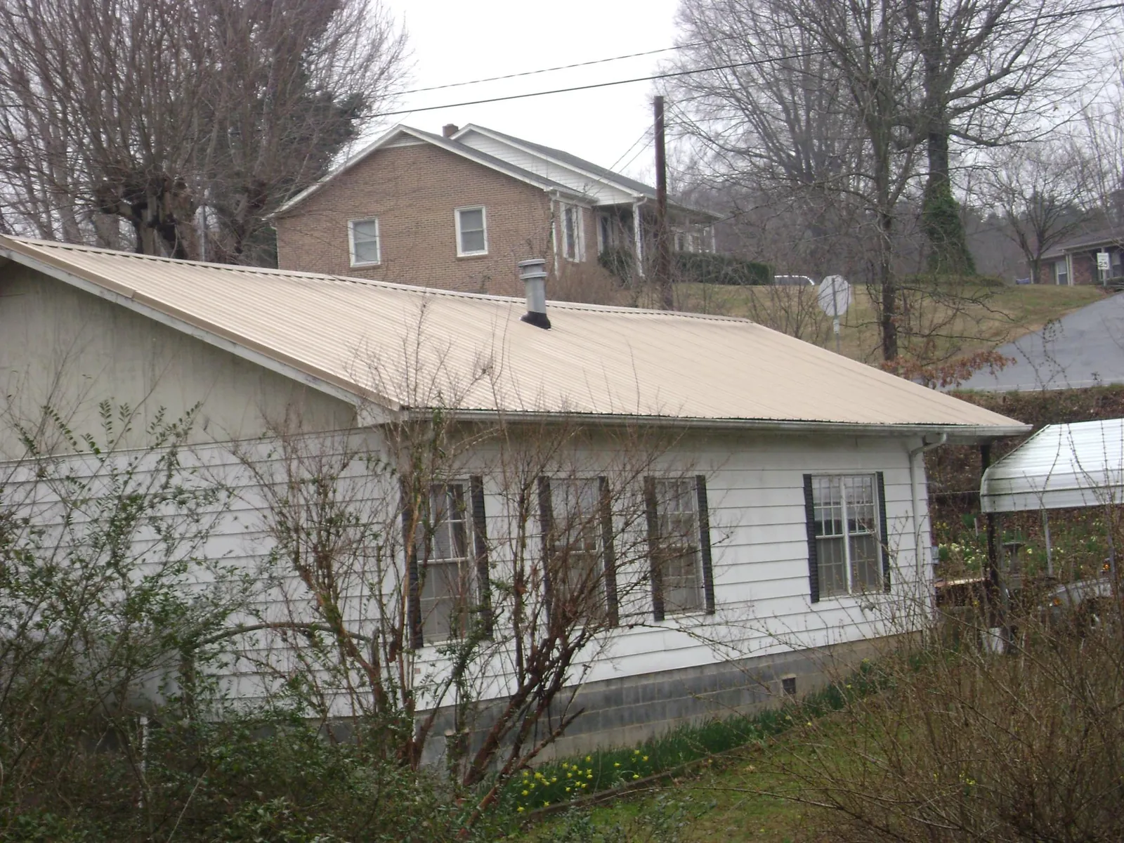 Tan metal roof on a white sided house set into a hillside — Commercial Roofing by Roofing Brothers in Walbridge